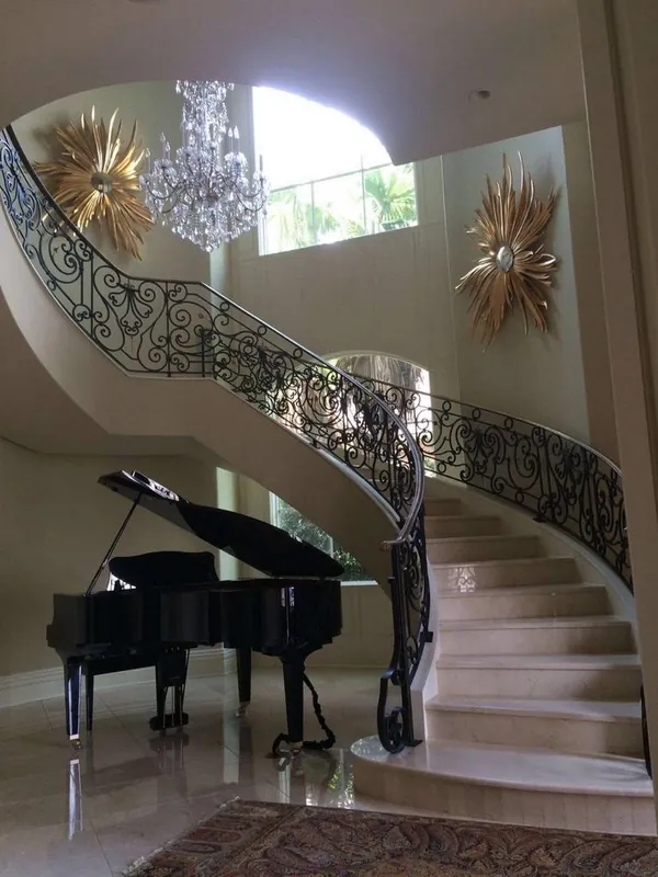 Escalera curva con baranda ornamental de hierro y un piano al pie.